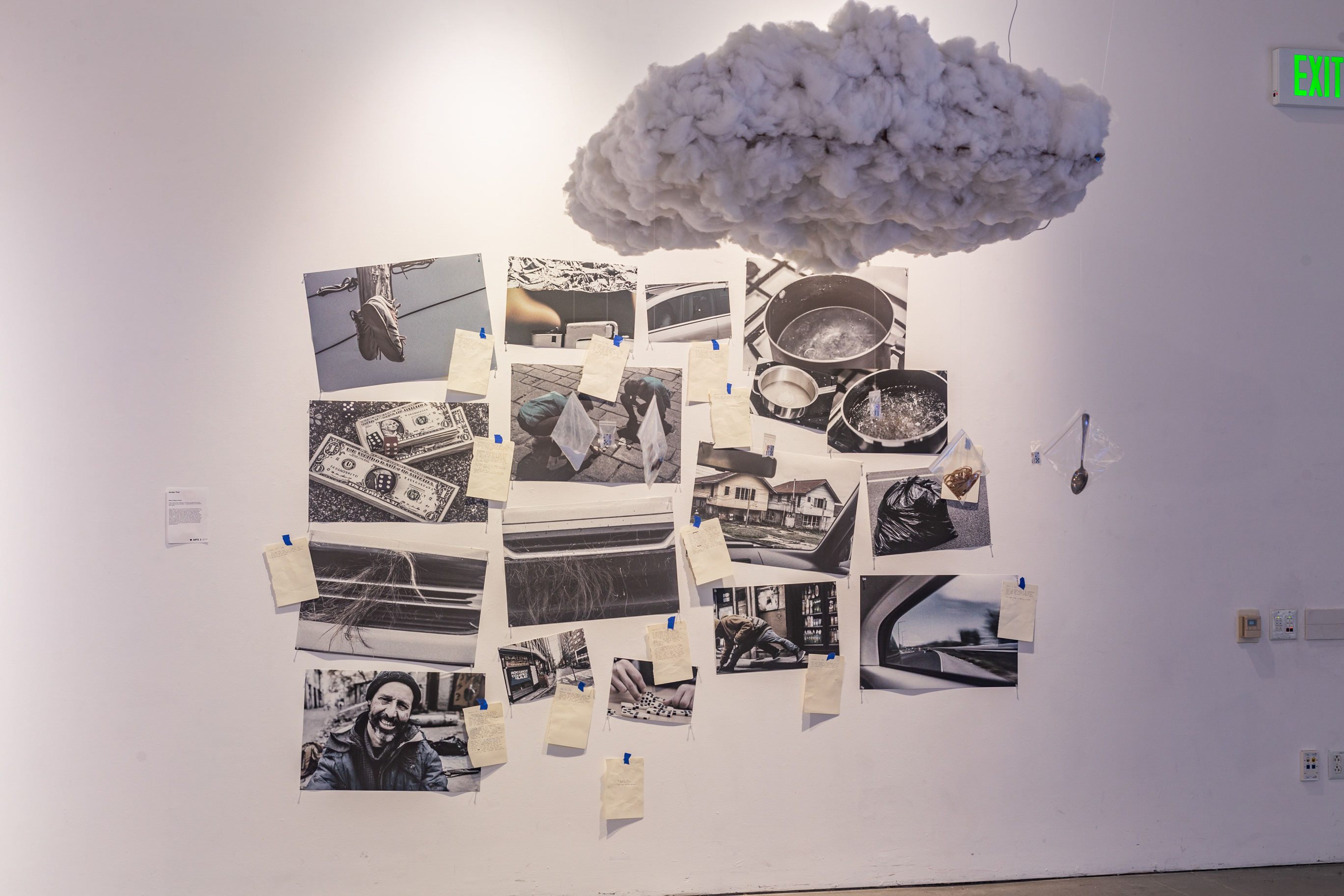 A white wall with a fabricated cloud above, on the wall are several AI-generated photo prints.